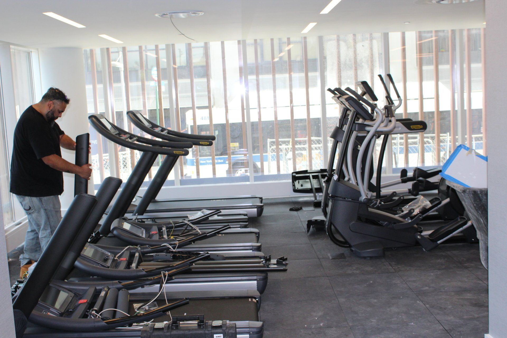 Man setting up exercise bikes and ellipticals at Quay Tower gym.