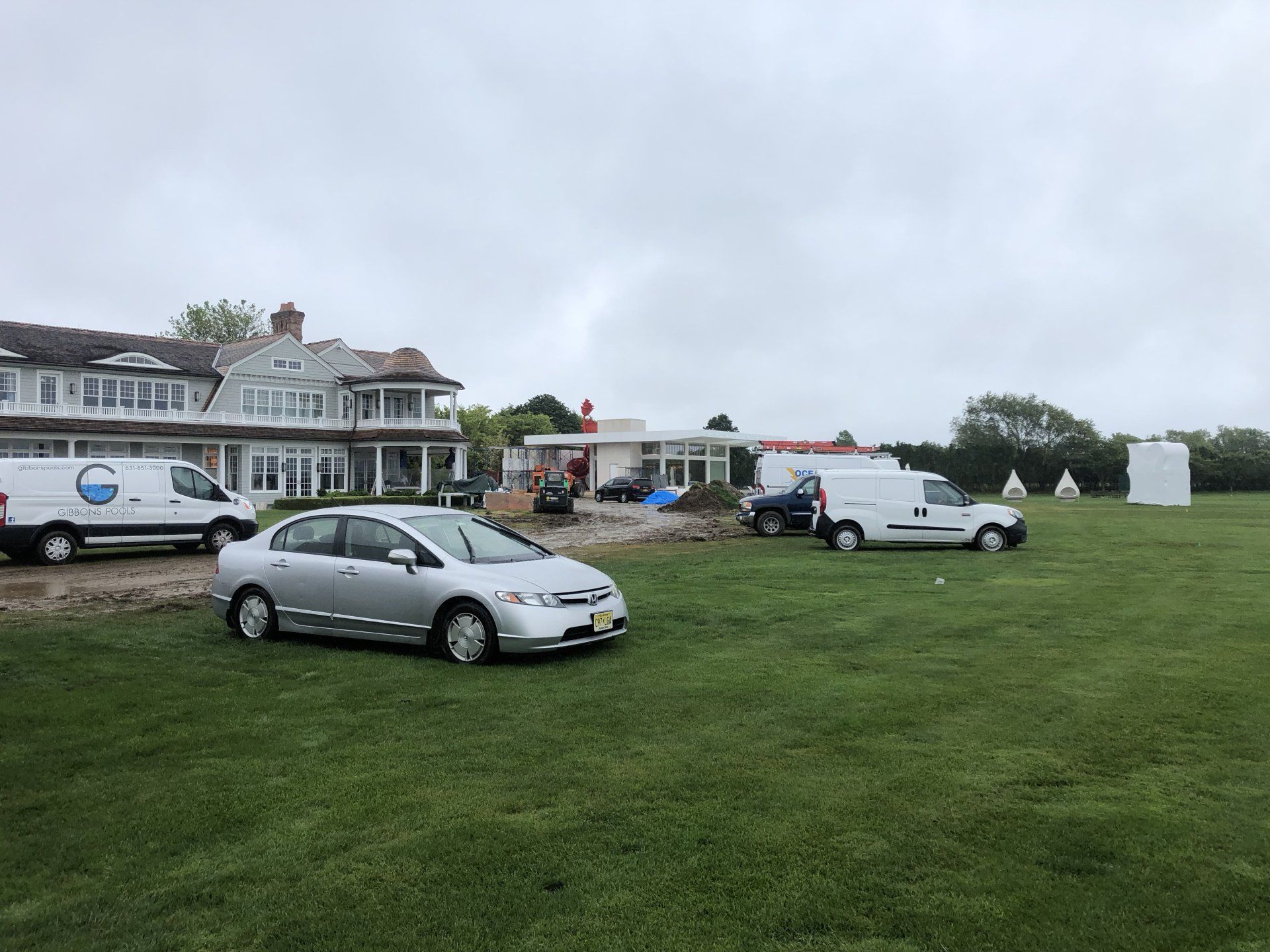 Luxury home exterior with cars and contractor vans parked on a green lawn.