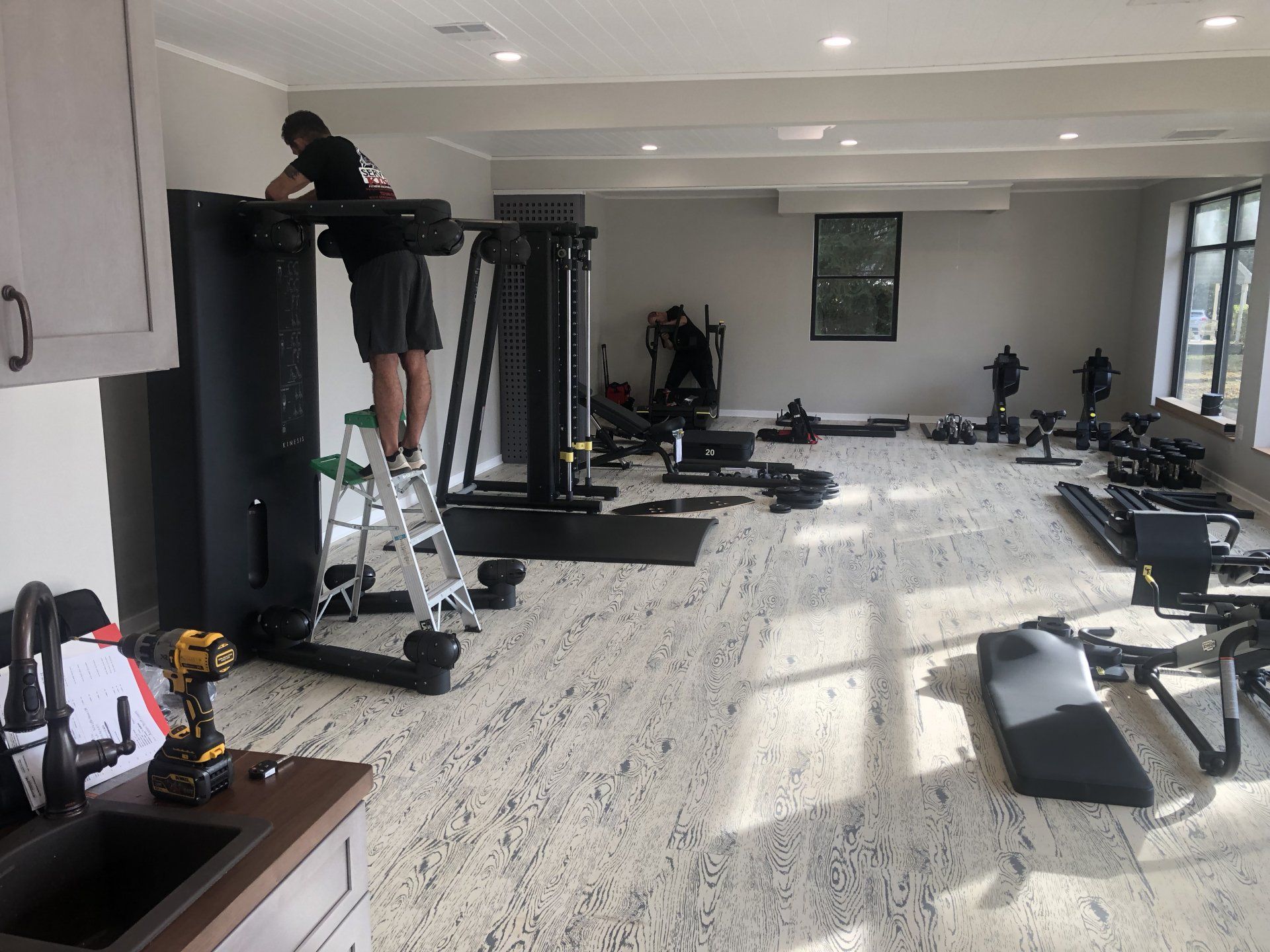 Worker adjusting exercise equipment during Daily Fitness gym setup.