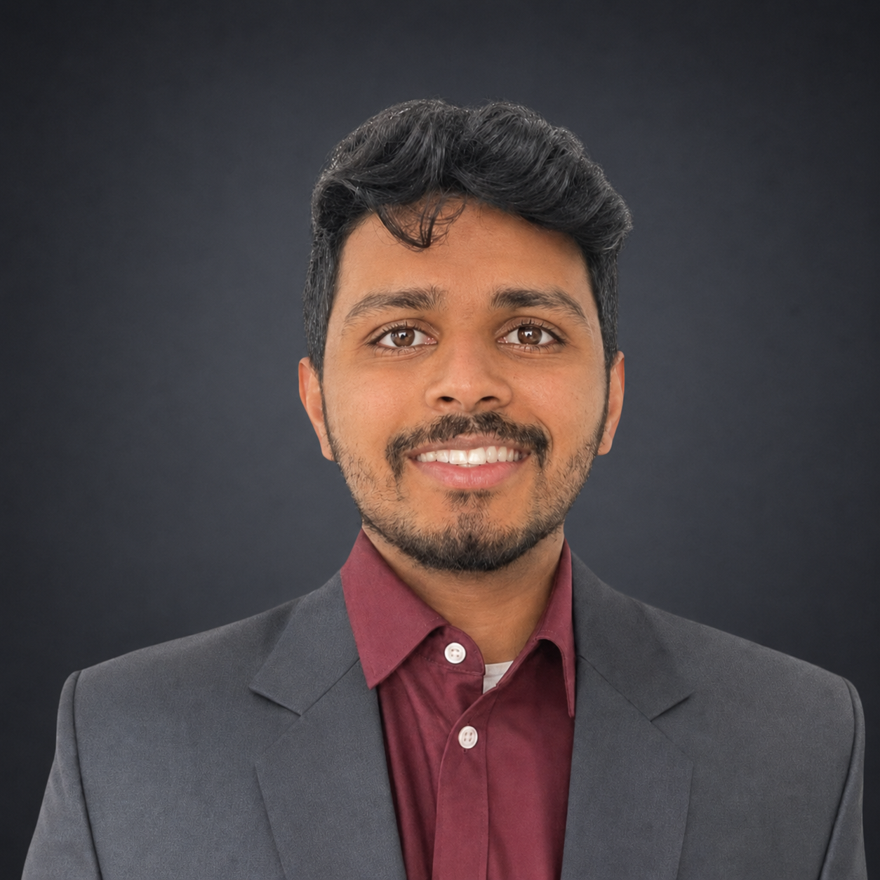 Man in suit smiling, burgundy shirt visible. White background.