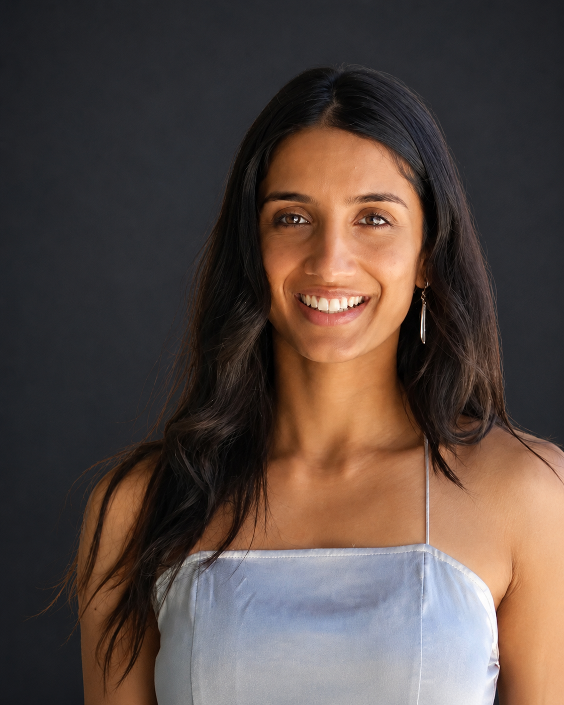 Woman smiling, looking to the side, wearing a light blue dress with thin straps.
