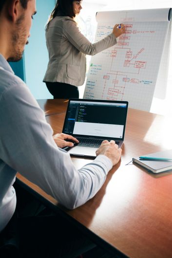 A man is using a laptop while a woman writes on a whiteboard.