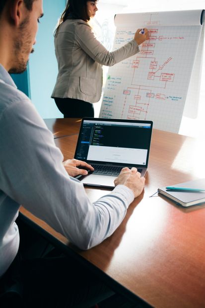 A man is using a laptop while a woman writes on a whiteboard.