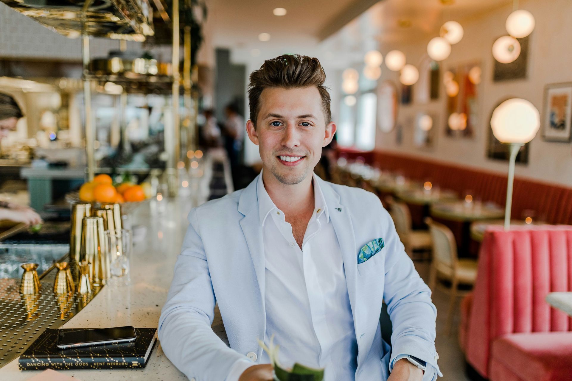 A man is sitting at a bar in a restaurant holding a drink.