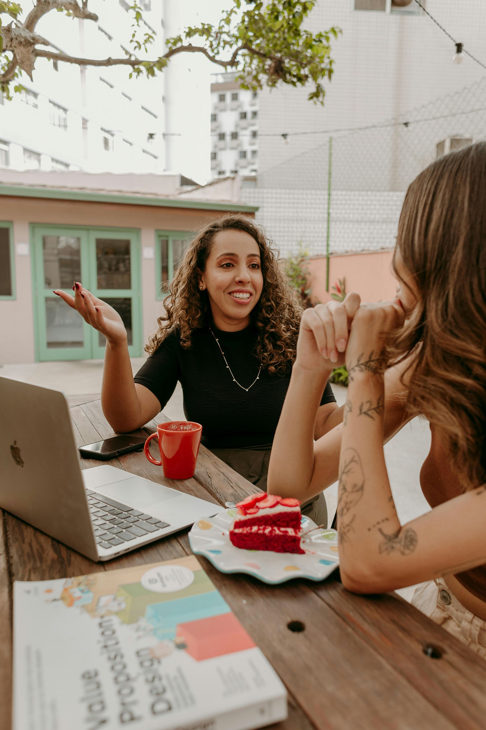 Two women are sitting at a table with a laptop and a book.