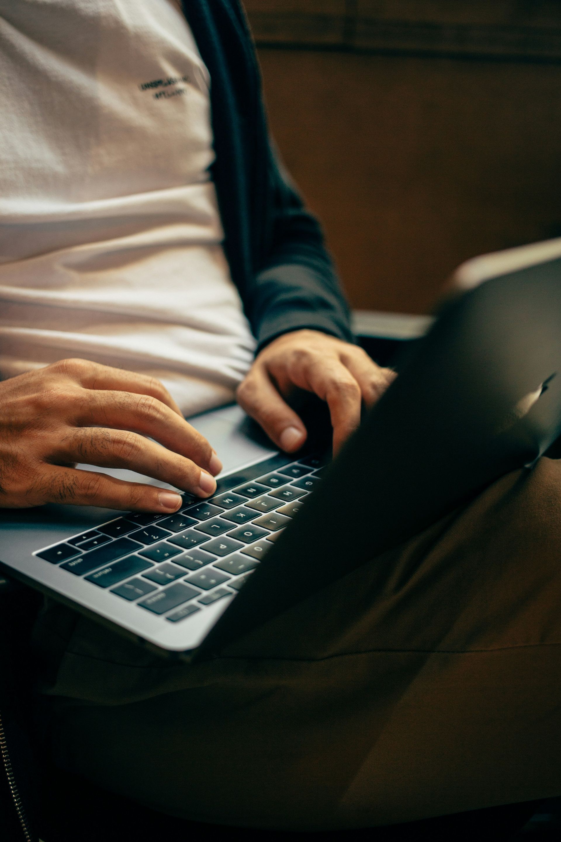 A man is typing on a laptop computer while sitting in a chair.