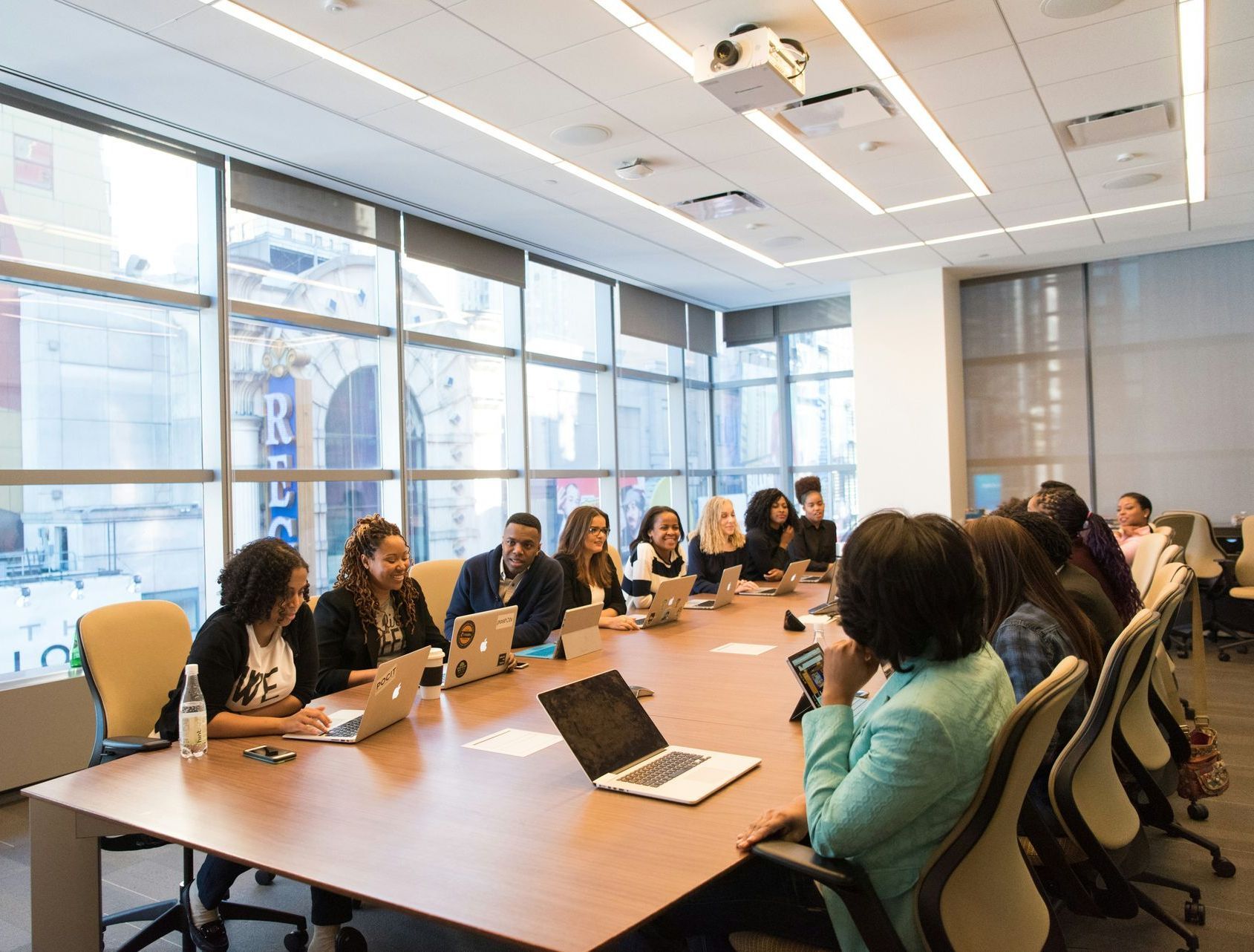 A group of people are sitting around a conference table with laptops.