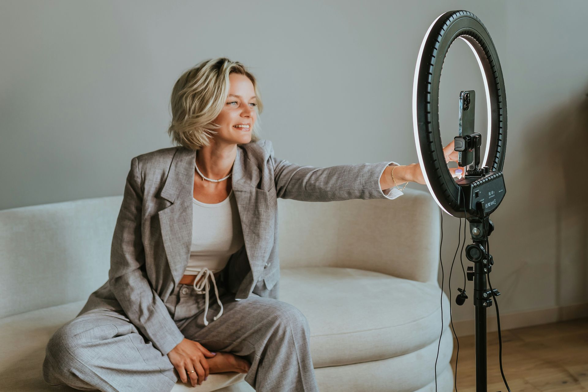 A woman is sitting on a couch taking a selfie with a ring light.