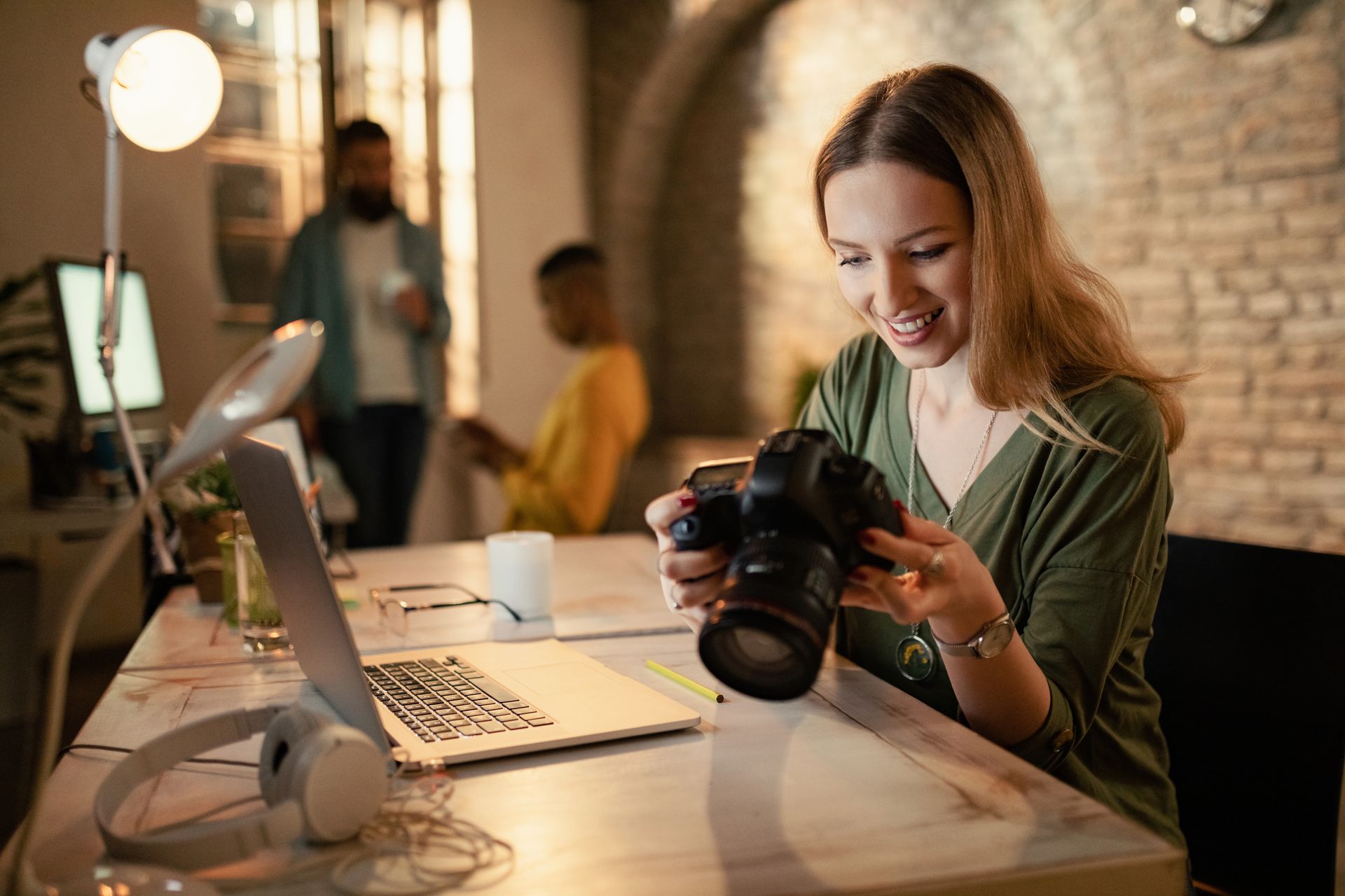 A woman is sitting at a desk taking a picture with a camera.