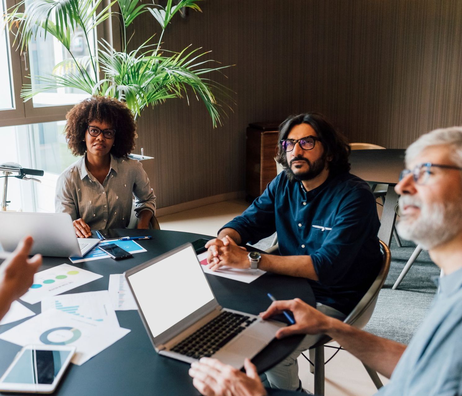 A group of people are sitting around a table with laptops.