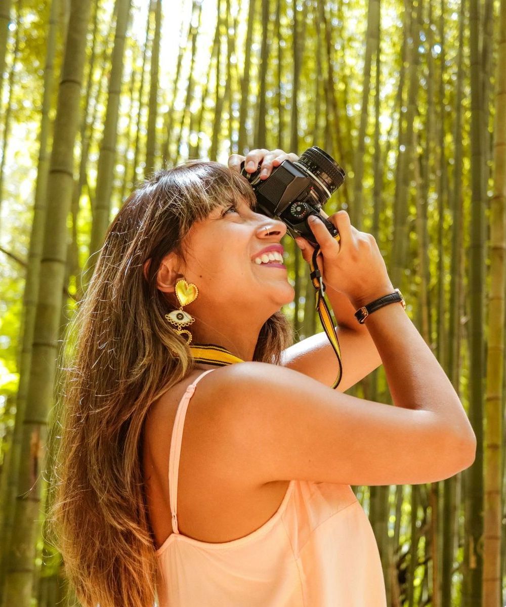 A woman is taking a picture with a camera in a bamboo forest.