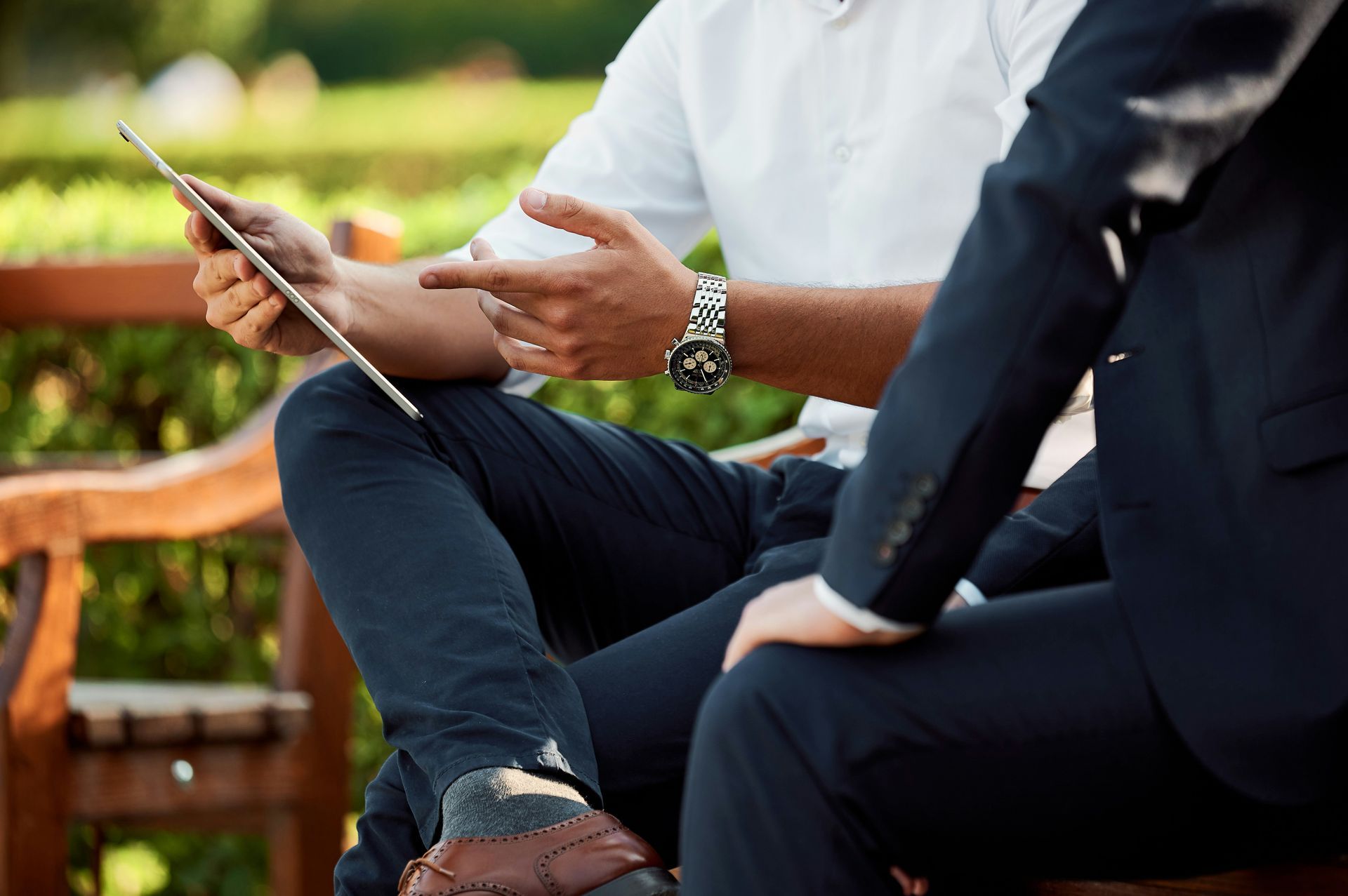 Two men are sitting on a bench looking at a tablet.