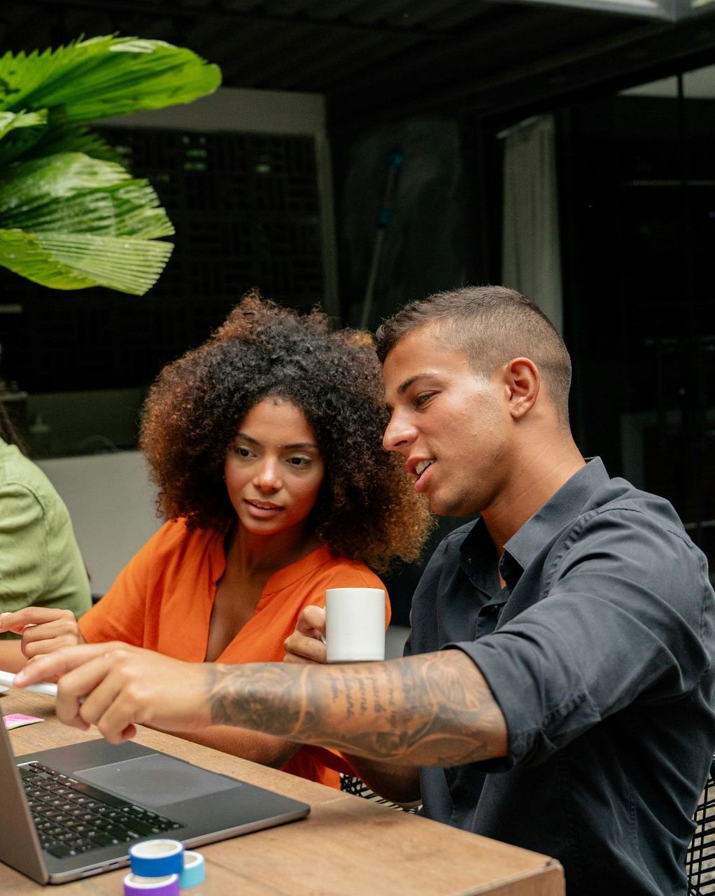 A man and a woman are sitting at a table looking at a laptop.