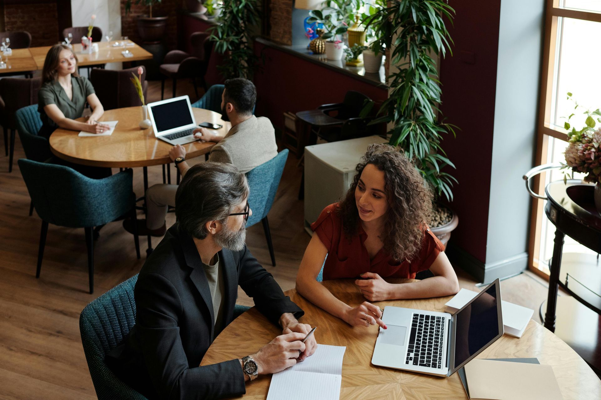 A man and a woman are sitting at a table in a restaurant with laptops.