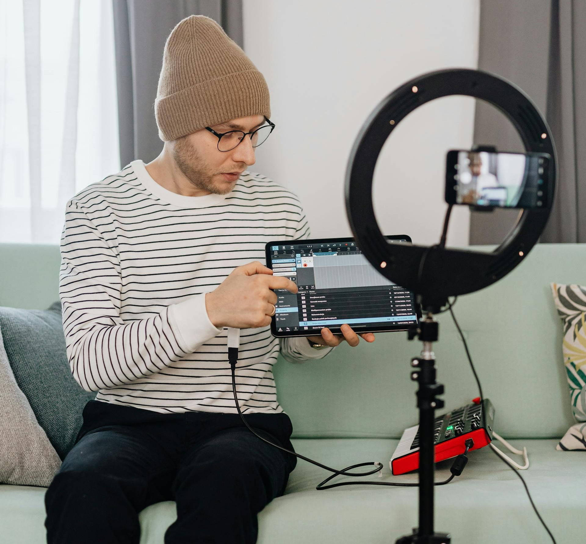 Man in beanie and glasses records a video tutorial on a tablet, using a ring light and smartphone.
