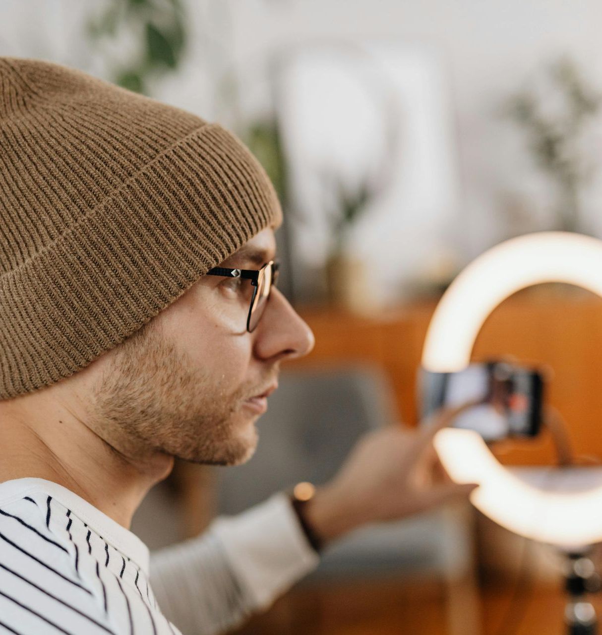 A man wearing a beanie and glasses is taking a picture with his phone
