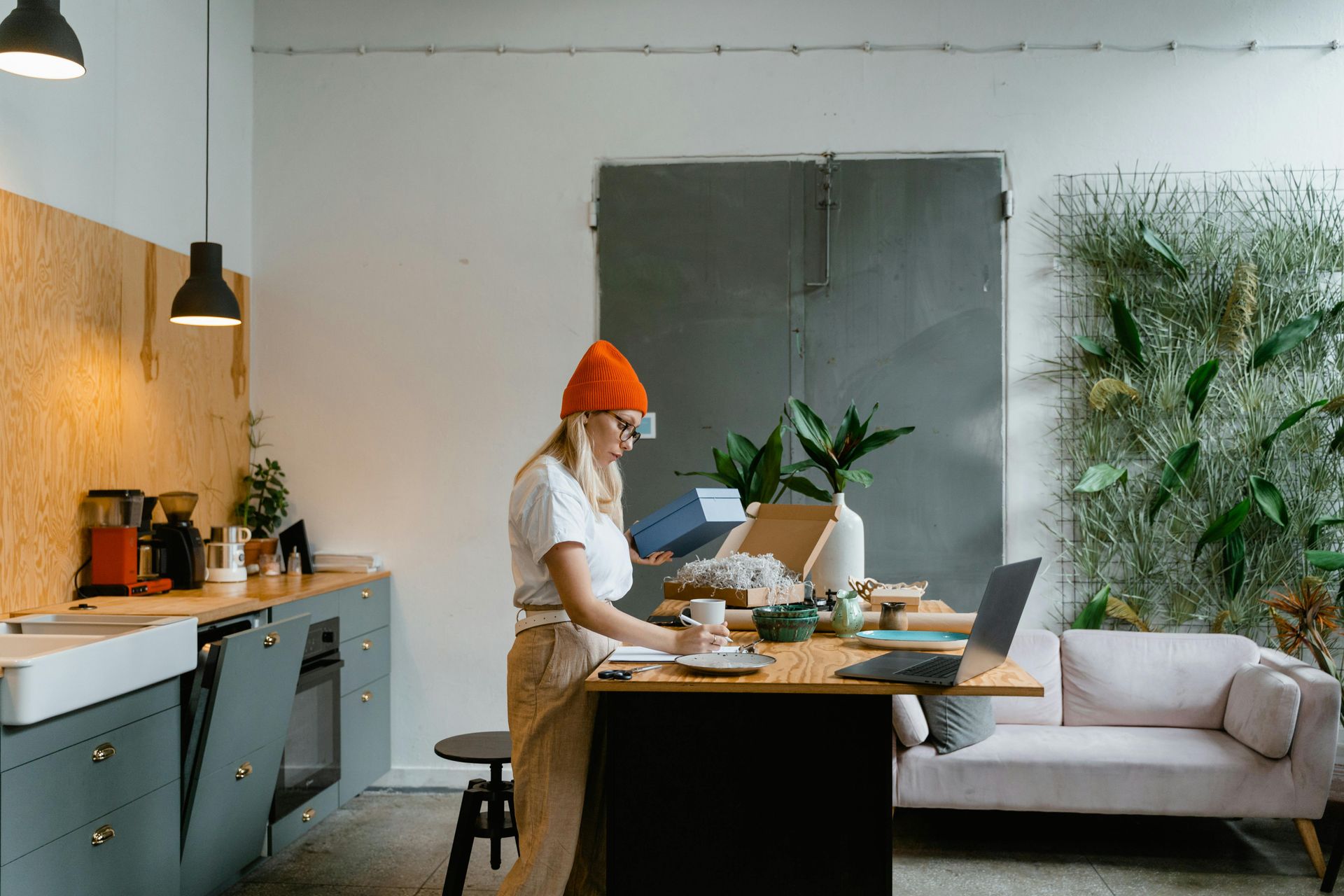 A woman is standing at a table in a kitchen with a laptop.