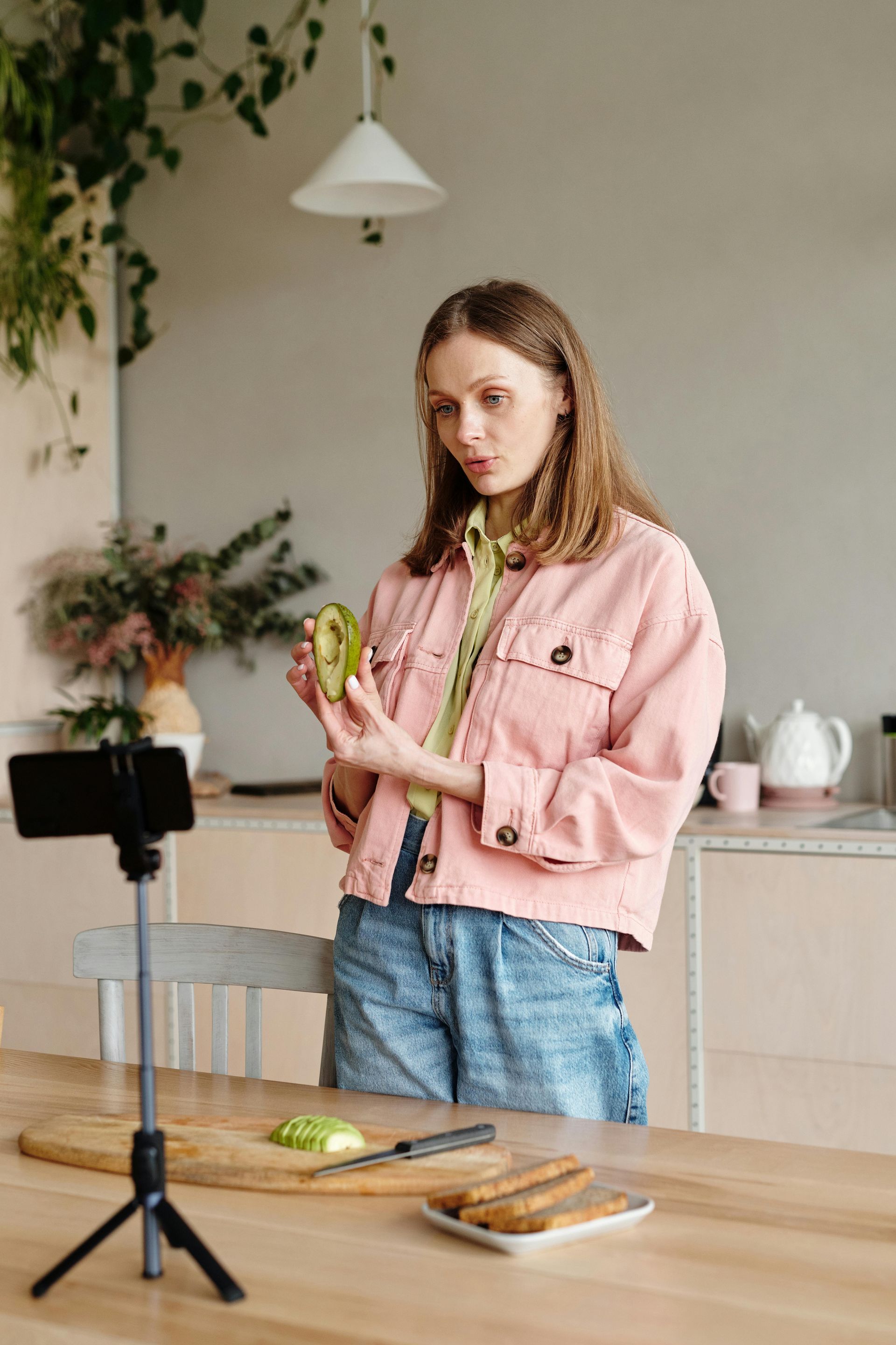 A woman in a pink jacket is standing in front of a table holding a green apple.