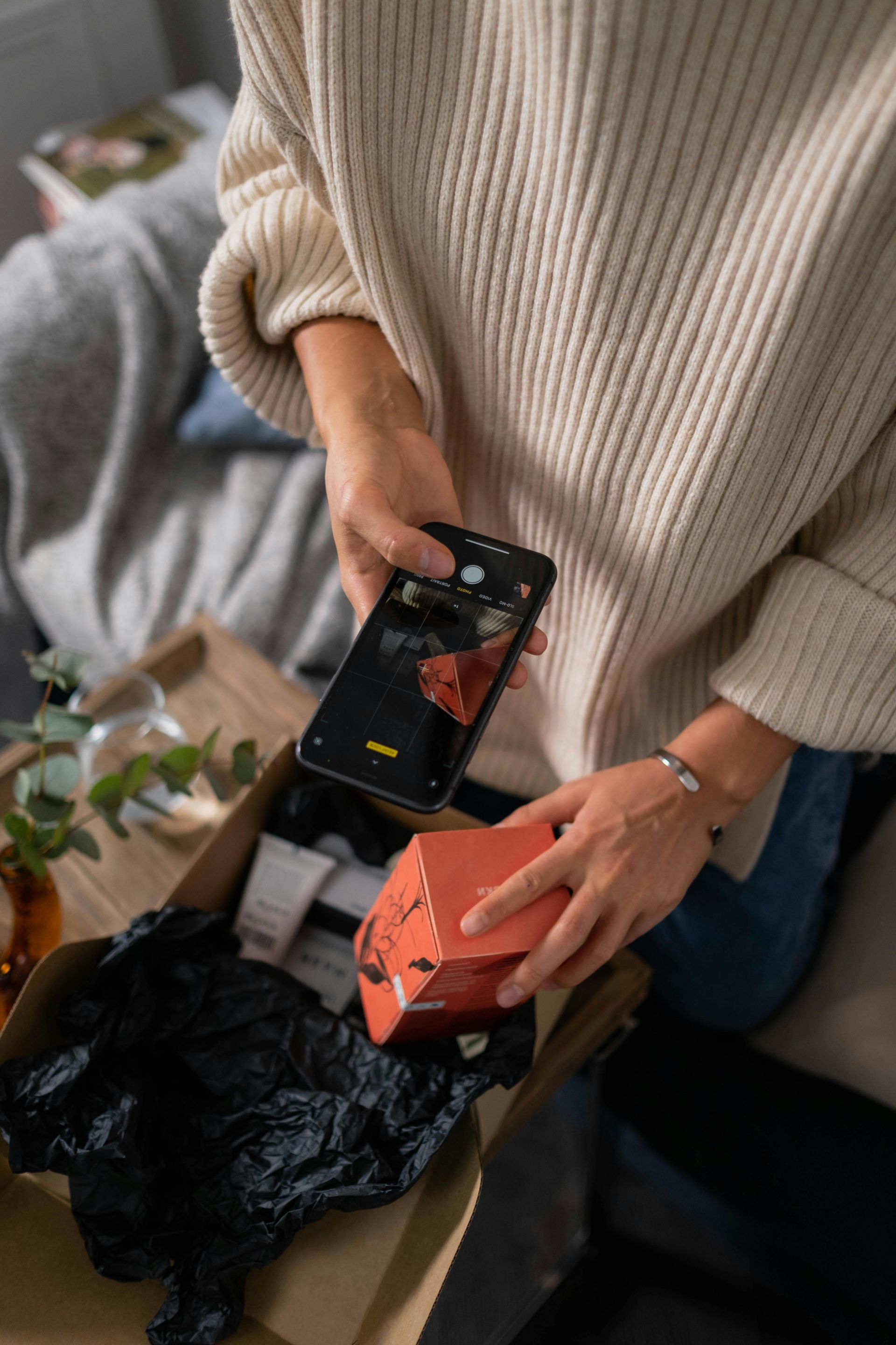 A woman is holding a cell phone over a box.