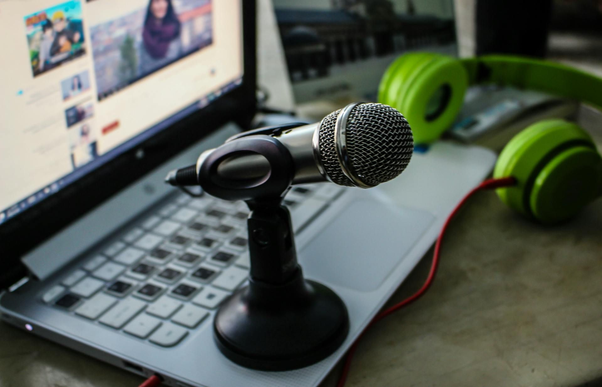 Microphone on laptop keyboard with green headphones; recording setup.