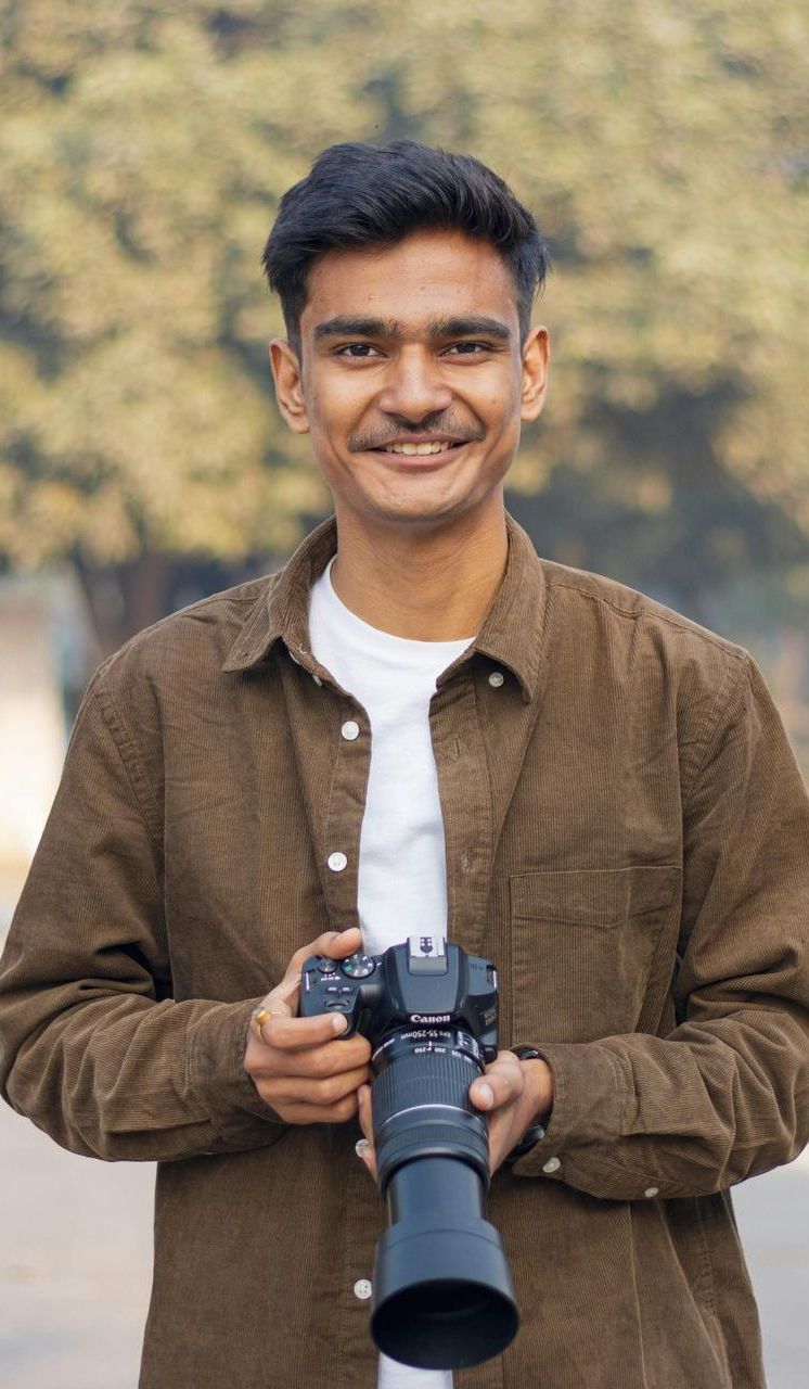 A young man is holding a camera in his hands and smiling.