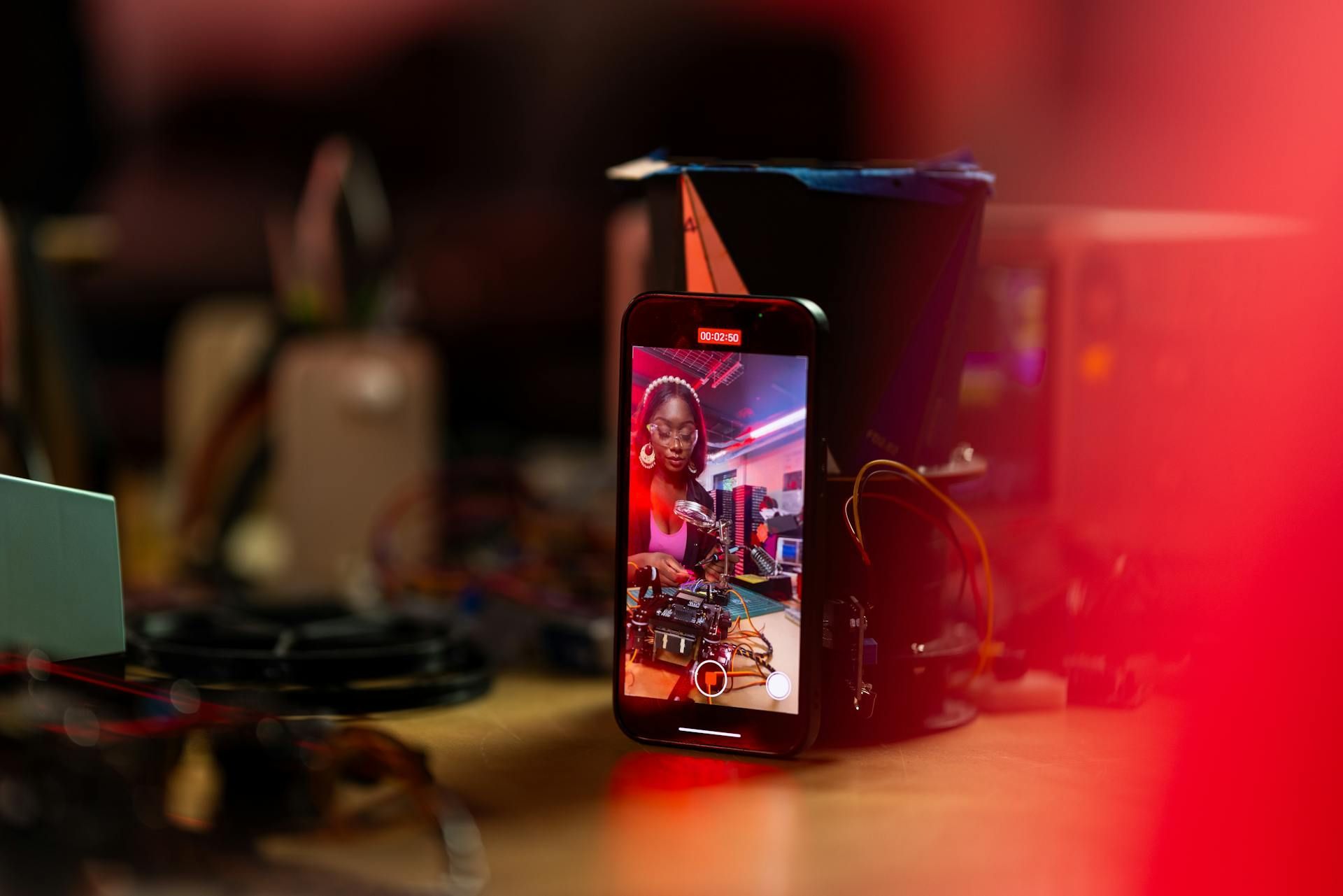 A phone filming a person in a colorful room; red light streaks across the foreground.