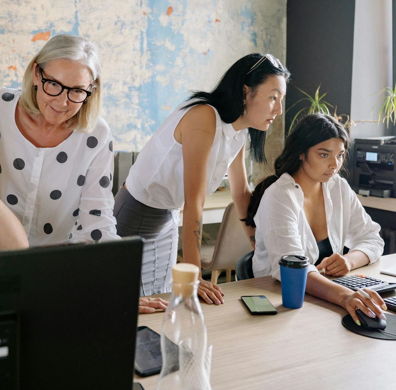 Three women are sitting at a table looking at a computer screen.