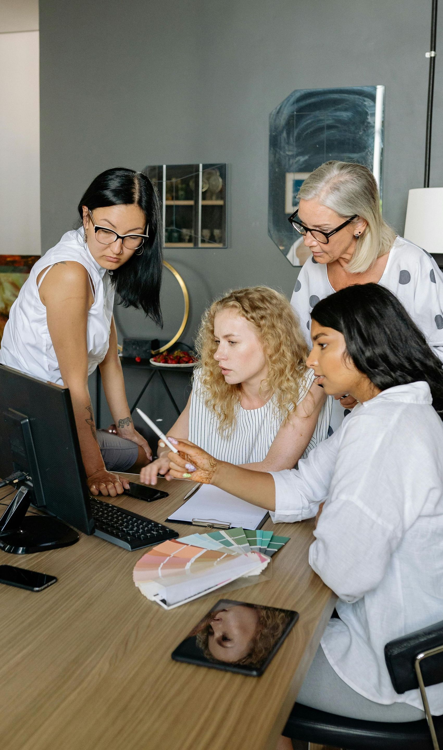A group of women are sitting around a table looking at a laptop.