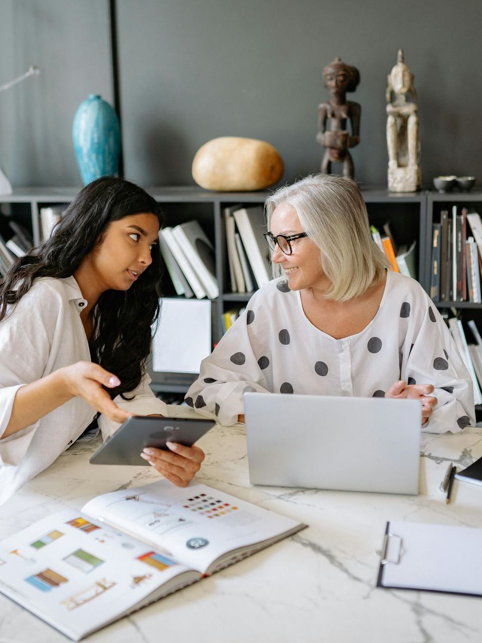 Two women are sitting at a table with a laptop and a tablet.