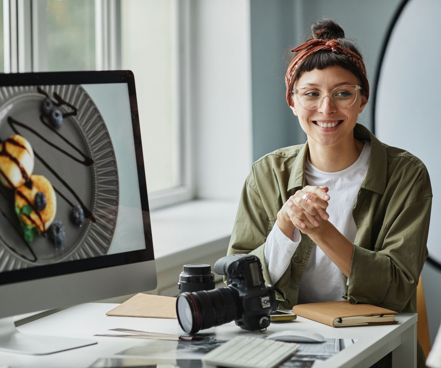A woman is sitting at a desk with a computer and a camera.