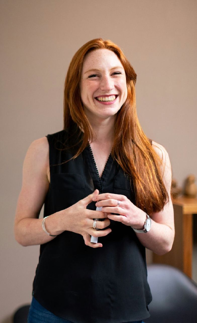 A woman with red hair is wearing a black tank top and smiling.