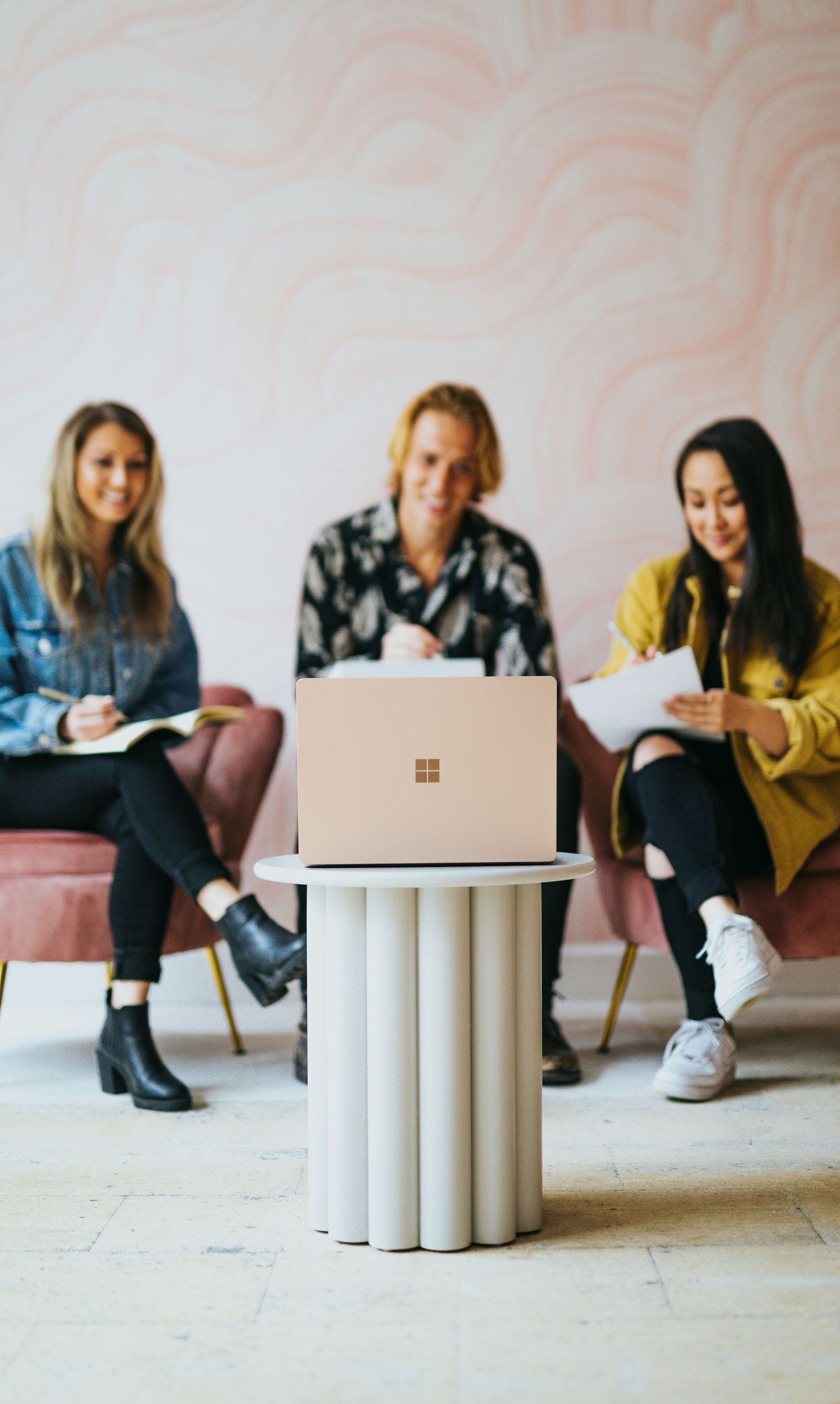 Three women are sitting in chairs with laptops on a table.