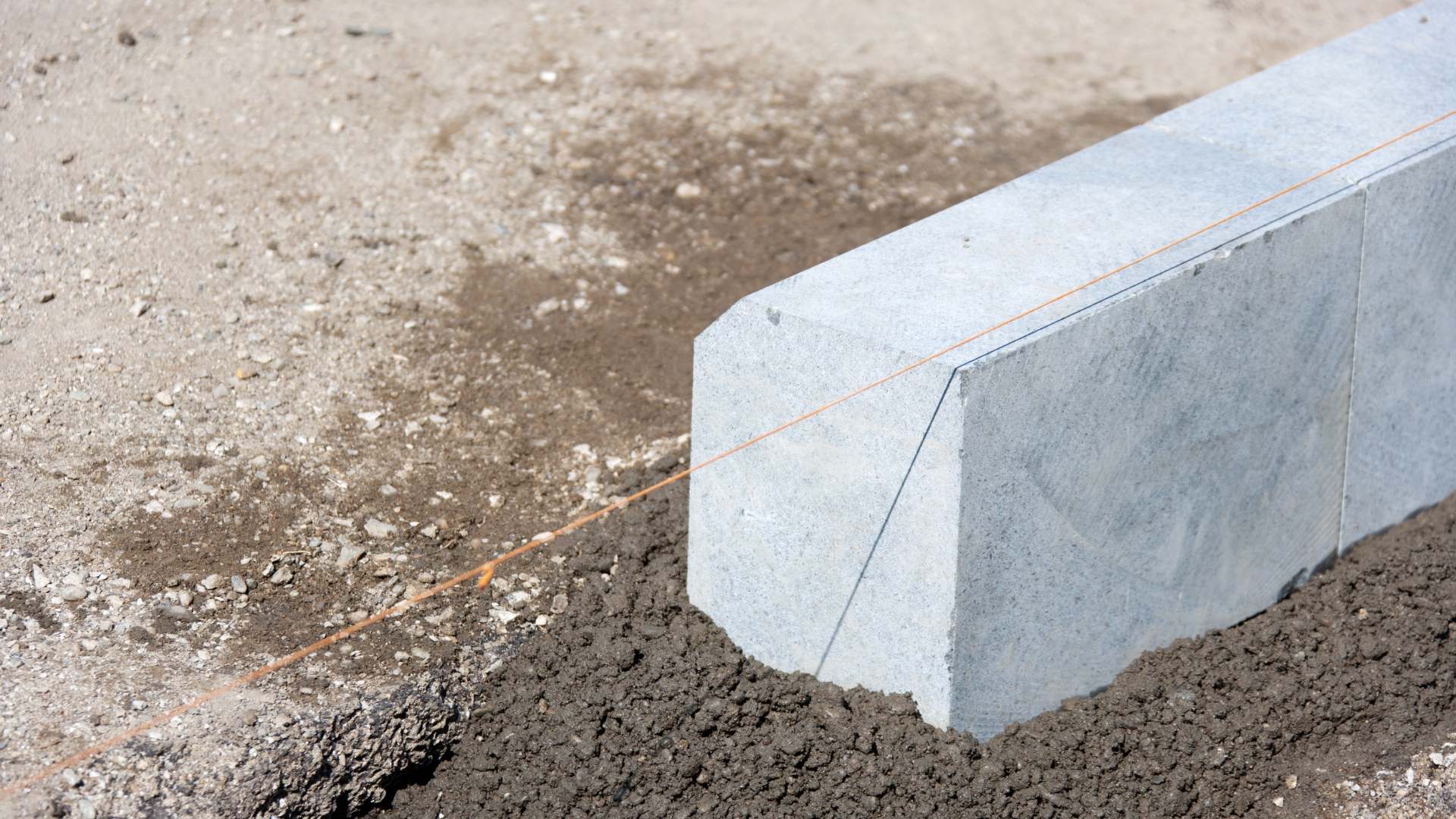 Concrete curb being installed on a dirt surface with wet mortar and string guide.