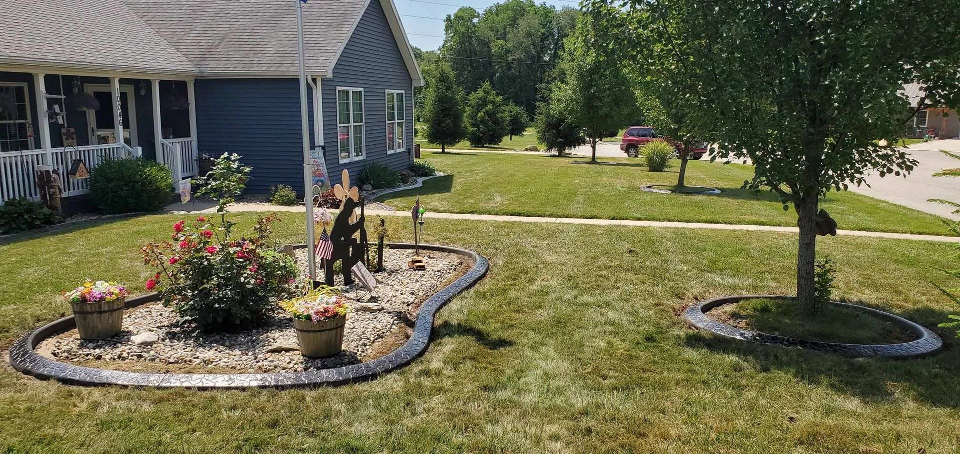 Blue house with flower beds and a tree in front. Green grass and a sunny day.
