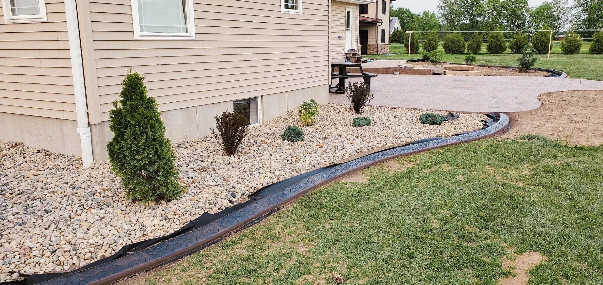 Landscaped yard with gravel bed, border edging, and plants near a building with a brick patio.