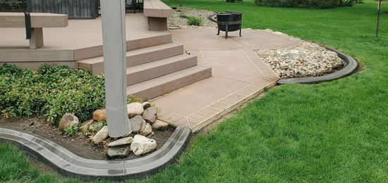 A patio with steps and fire pit surrounded by a stone border. Green grass in the foreground.