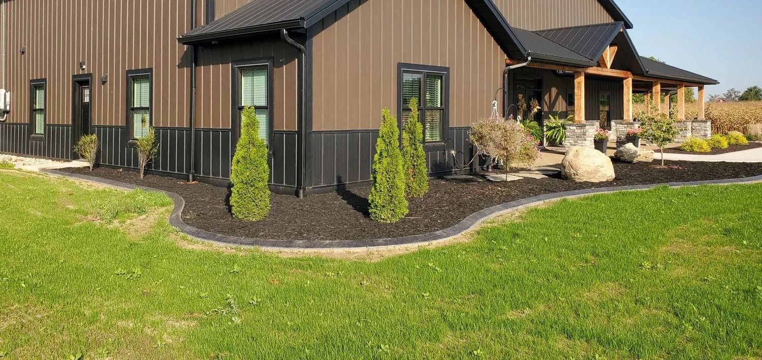 Brown building with black trim, green lawn, and landscaping with shrubs.