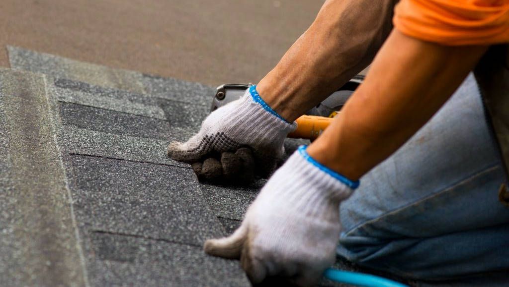 A man wearing gloves is working on a roof.