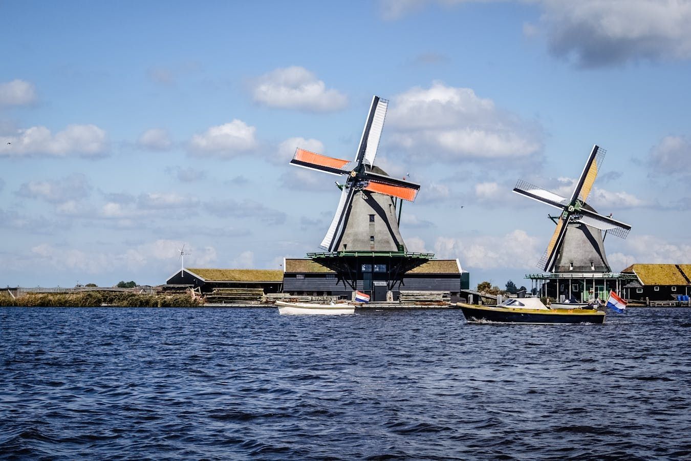 Two windmills with orange and yellow blades on a body of water under a blue sky.