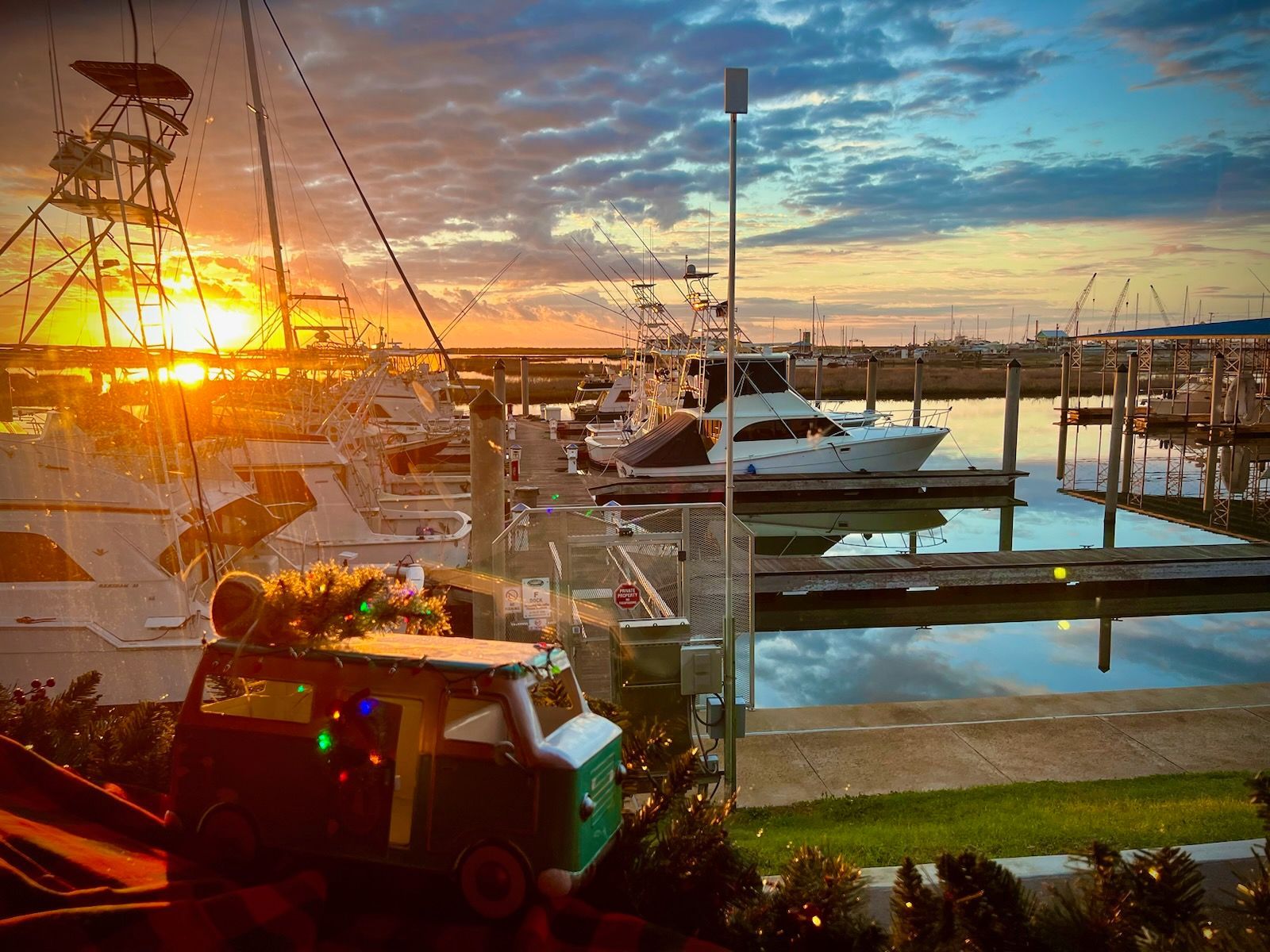A sunset over a marina with boats docked and a tractor decorated with christmas lights.