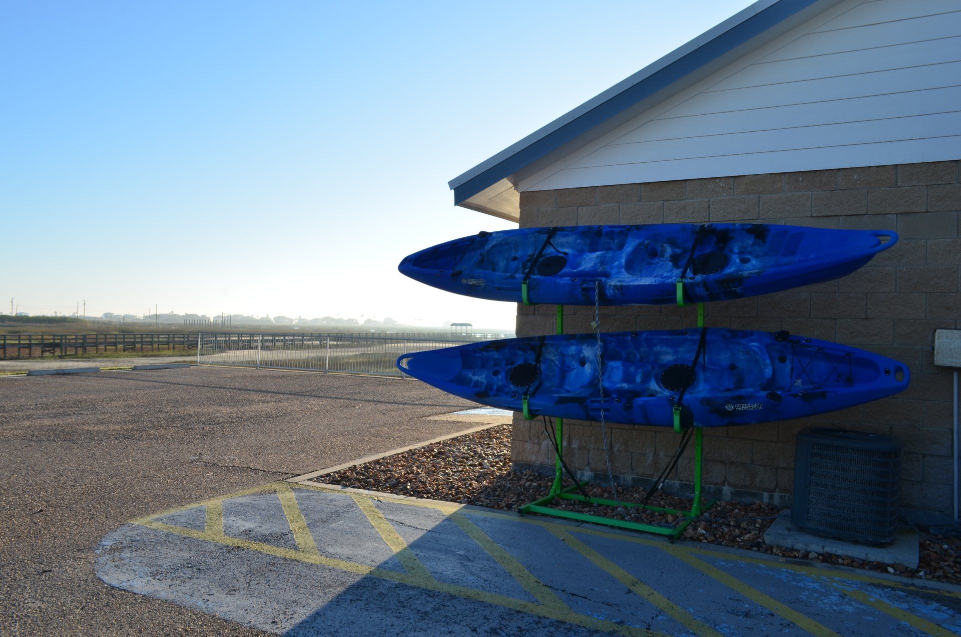 Two blue kayaks are sitting on a green rack on the side of a building.