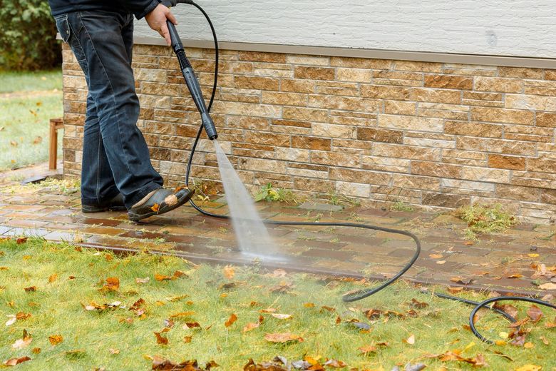 Person pressure washing a brick wall and grassy area.