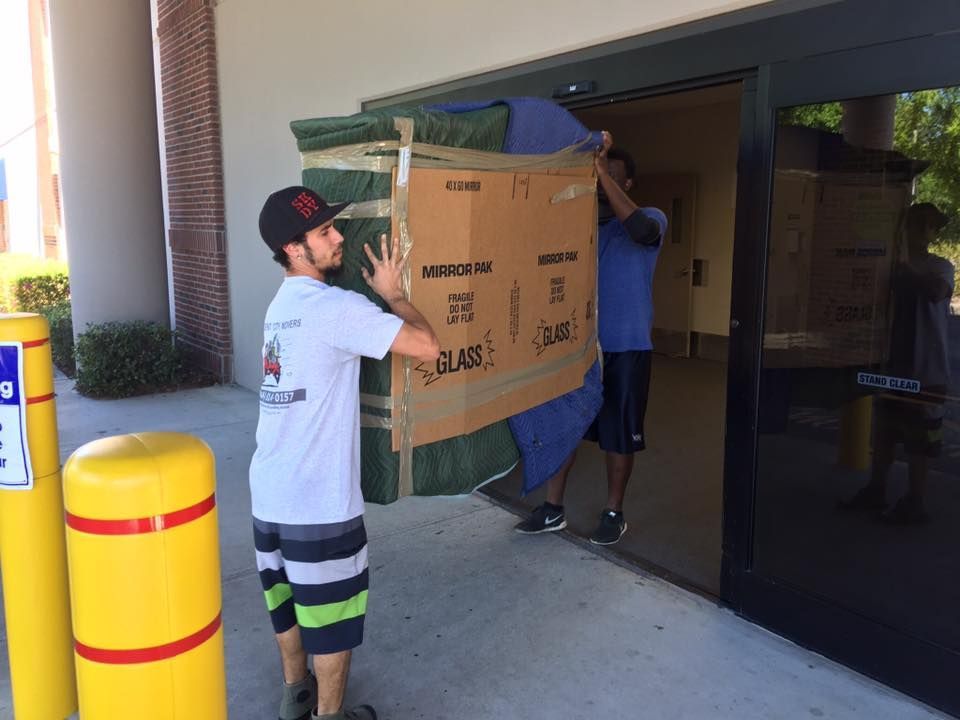 Two men are carrying a large cardboard box into a building.
