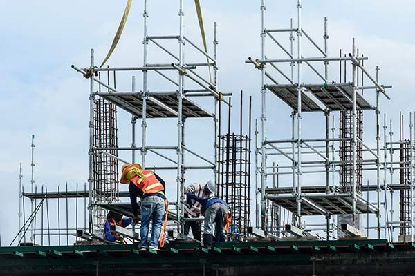 Construction workers on scaffolding beside a building frame, wearing safety vests and helmets