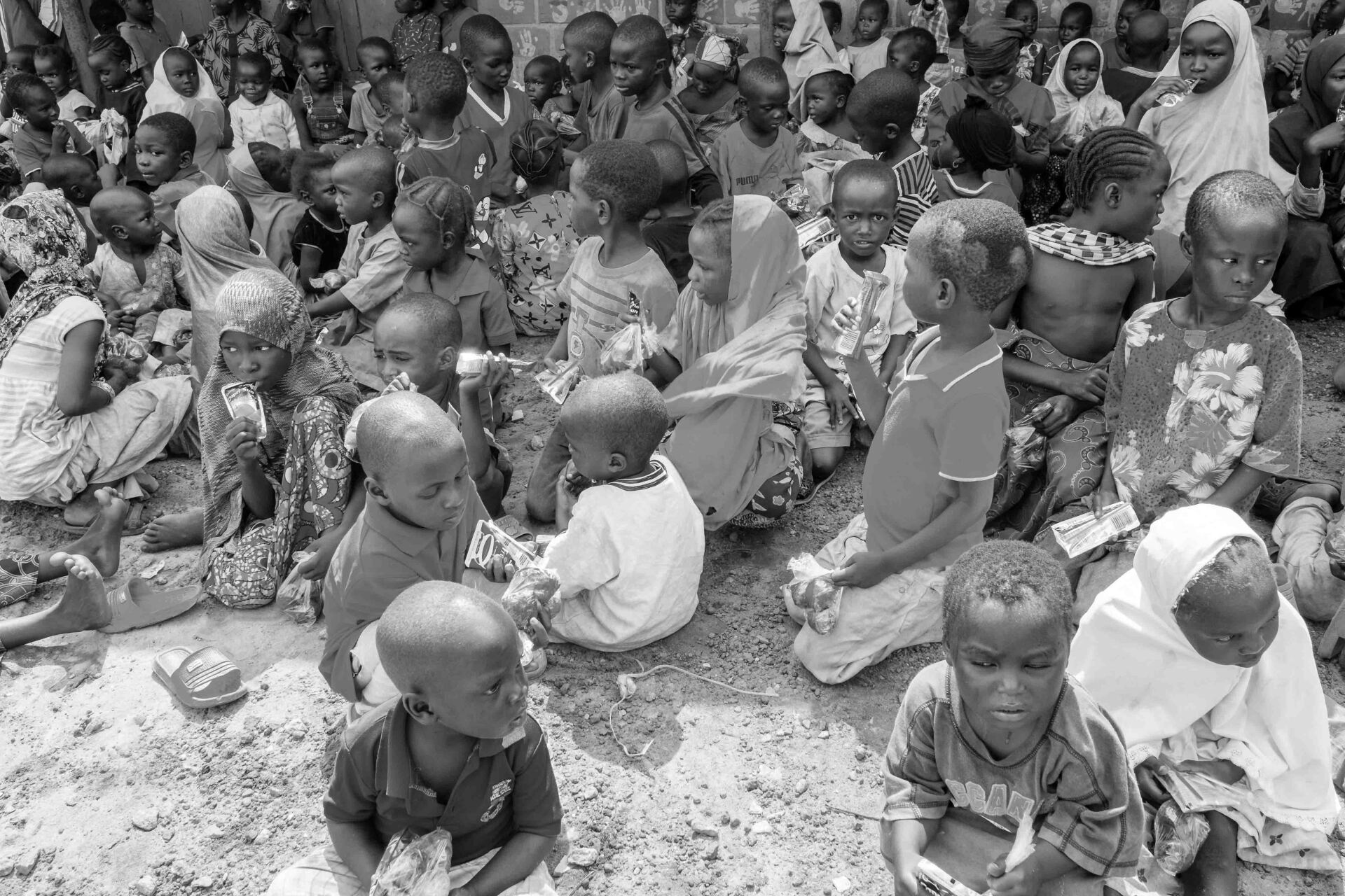 Auf einem Schwarzweißfoto sitzt eine große Gruppe Kinder auf dem Boden.