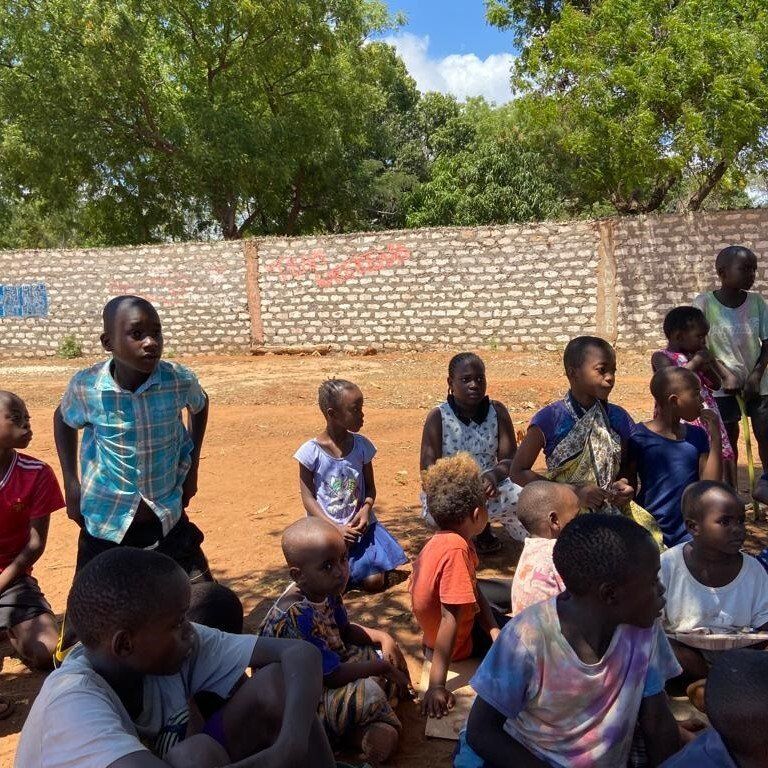 Eine Gruppe von Kindern sitzt auf dem Boden vor einer Backsteinmauer
