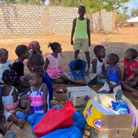 Eine Gruppe Kinder sitzt vor einer Backsteinmauer auf dem Boden.