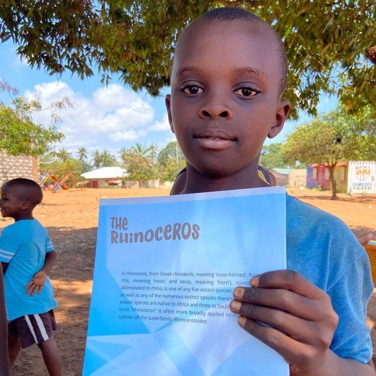 Ein kleiner Junge hält ein Stück Papier mit der Aufschrift „Das Nashorn“