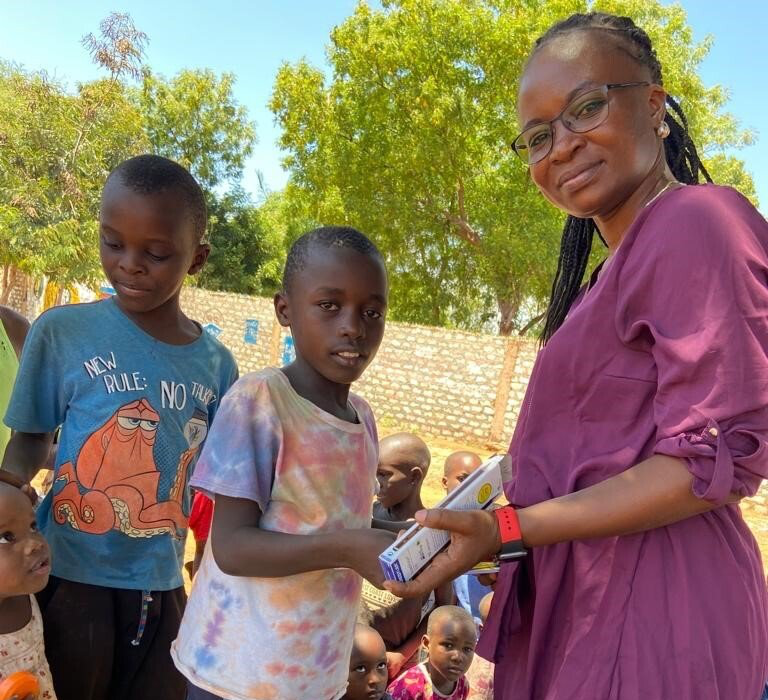 Eine Frau in einem lila Kleid hält vor einer Gruppe von Kindern ein Buch.