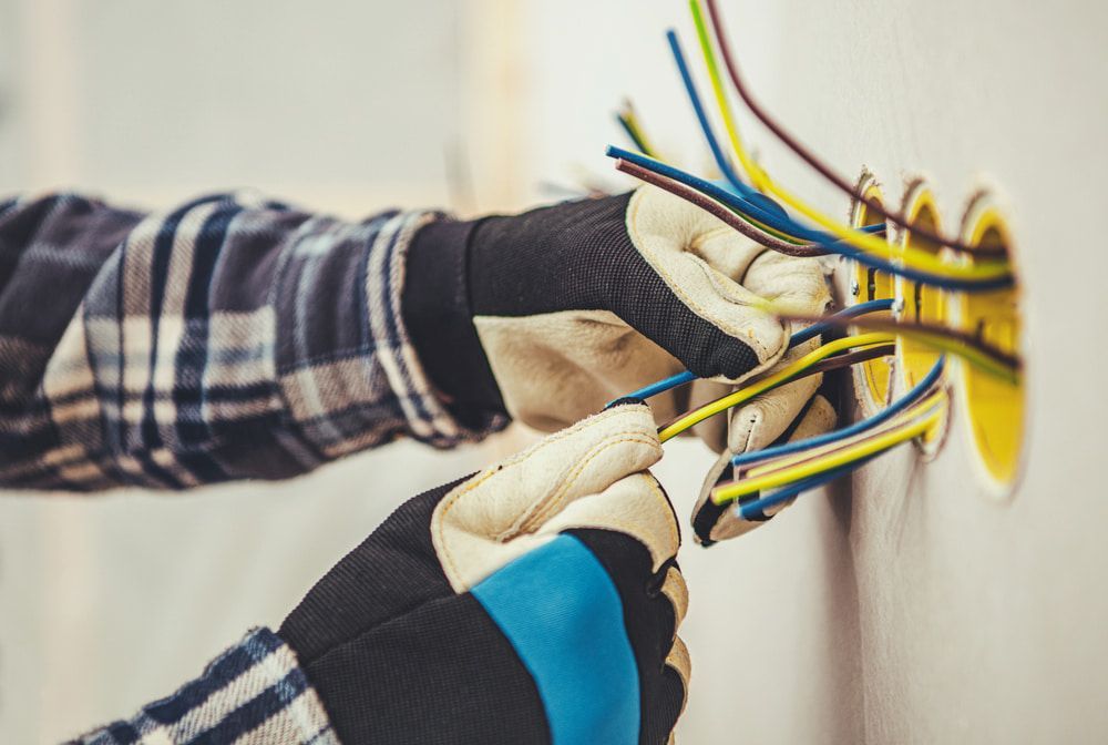 Electrician's Hands Wearing Gloves Connecting Wires Into a Wall Outlet — Darwin Electrical Services in Humpty Doo, NT